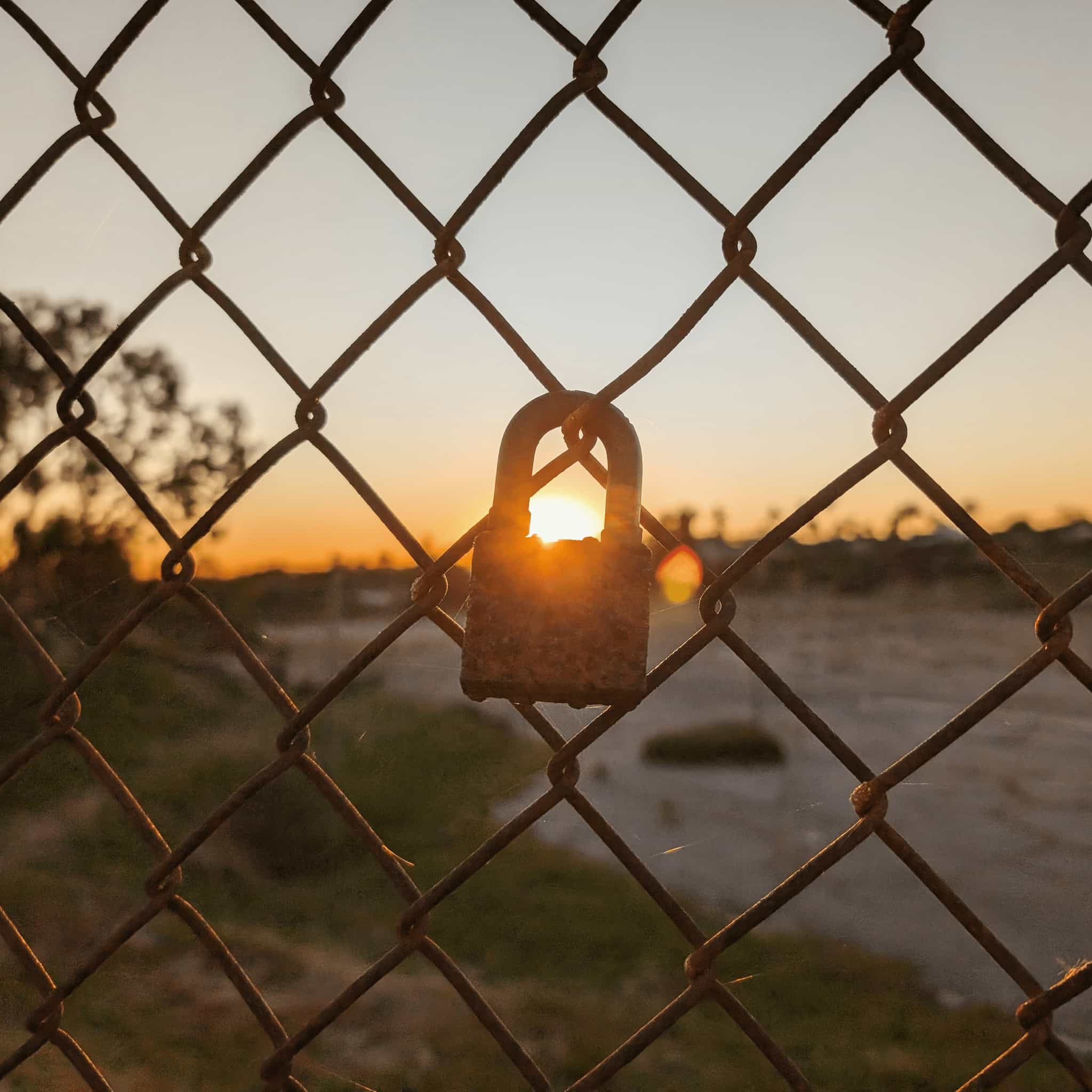 A sunset showing through a rusty lock on a rusty chain link fence.