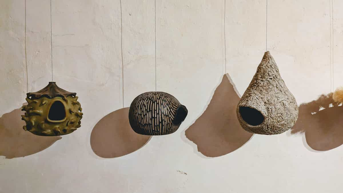 Three bird houses that are shaped like round homes hang in front of a white wall, casting shadows.