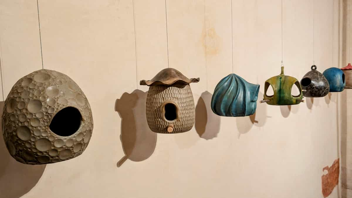 Six more creative bird houses hang next to a wall, some with vibrant colors.