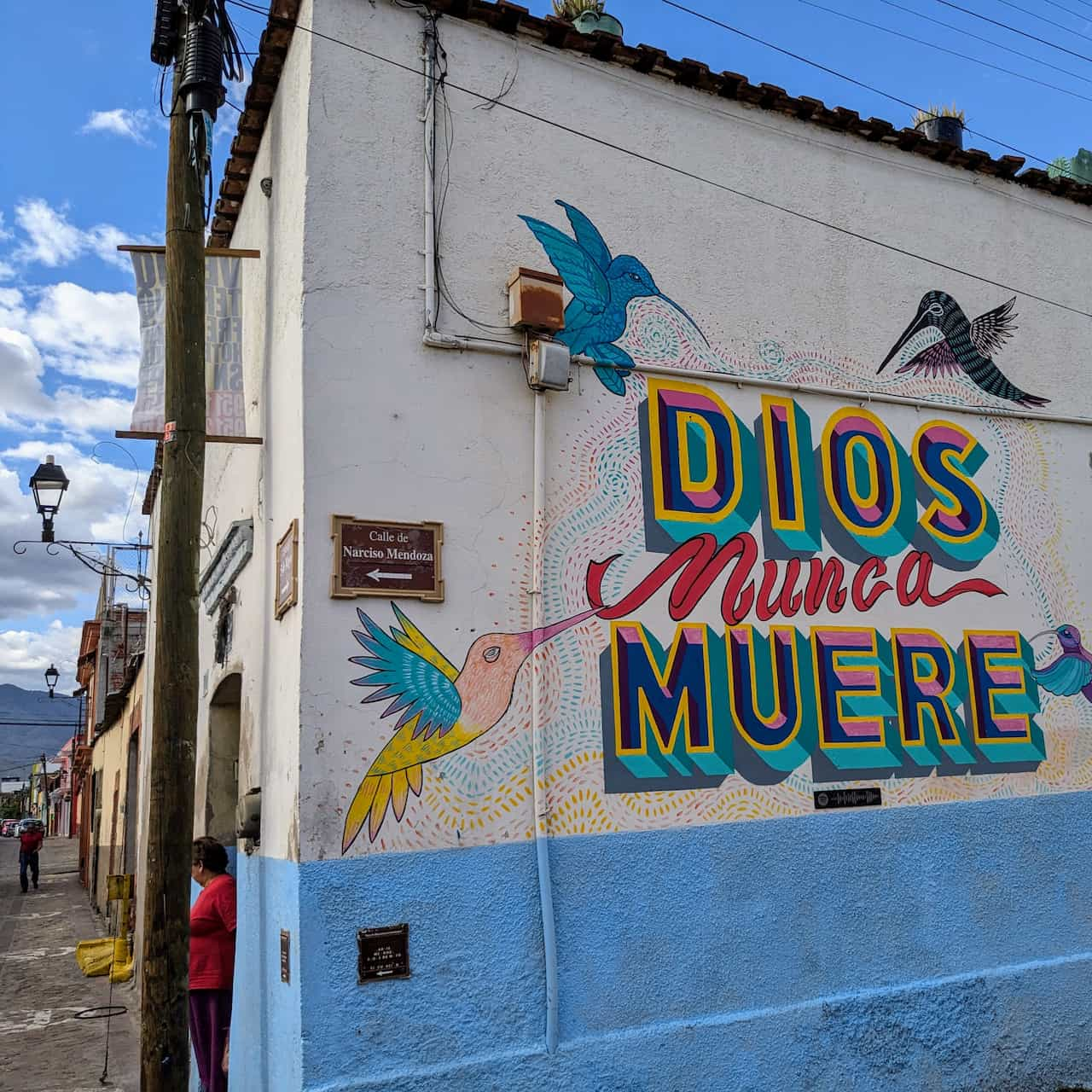 Colorful mural of hummingbirds around the words 'Dios nunca muere' on the corner of a building.