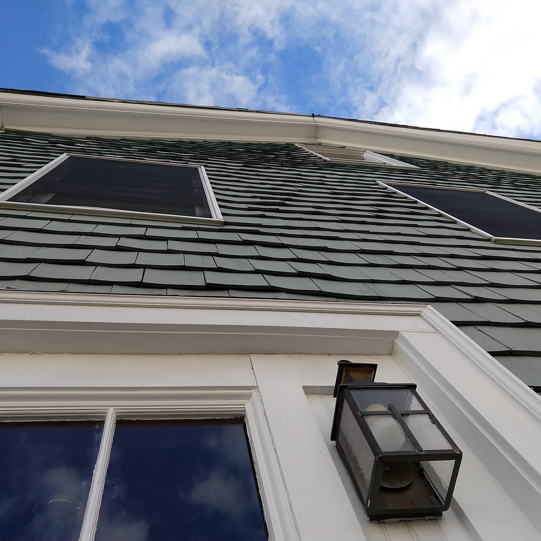 Looking up at the front of a colonial style building with cedar shingle siding painted light green.