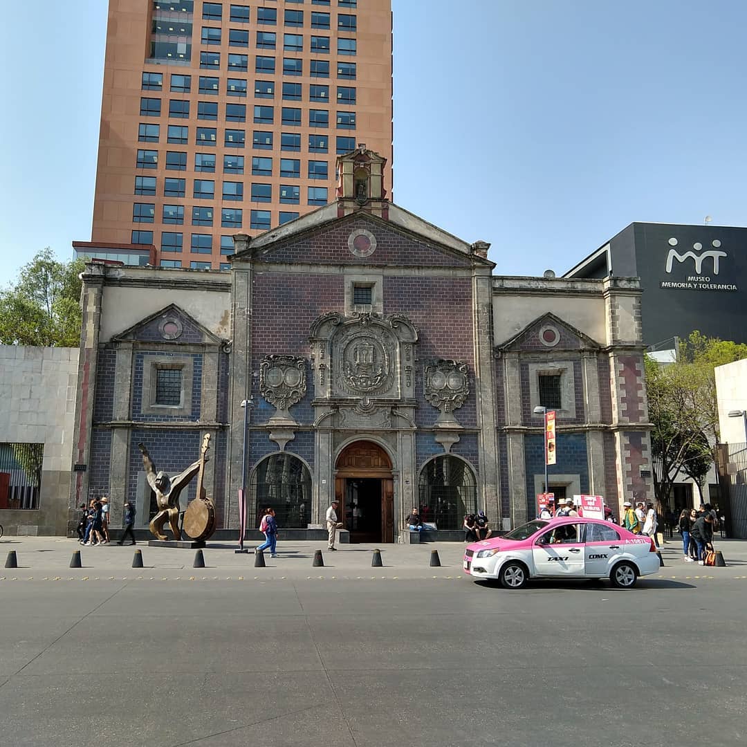 Looking at the face of an old, yet ornate brick building. In front is a pink taxi and a statue of a gorilla holding a banjo. To the right and behind are more modern, taller buildings.