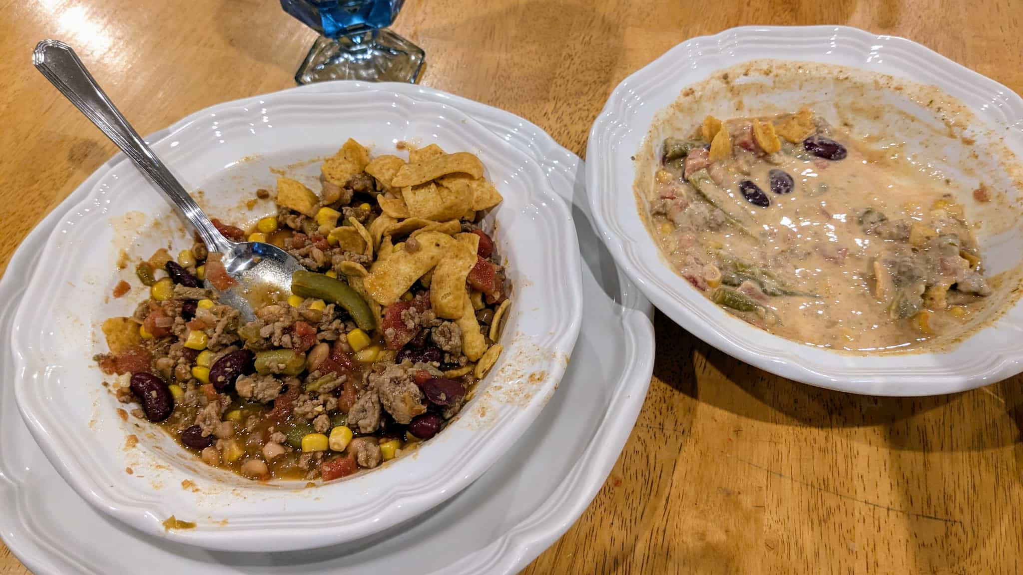 Two bowls with a beef and vegitable soup topped with corn chips. One bowl's contents are nearly white with added cream.