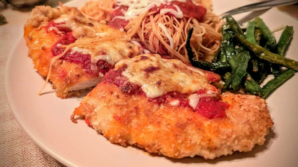 Plate with breaded chicken covered in tomato sauce and cheese served with spaghetti and green beans.