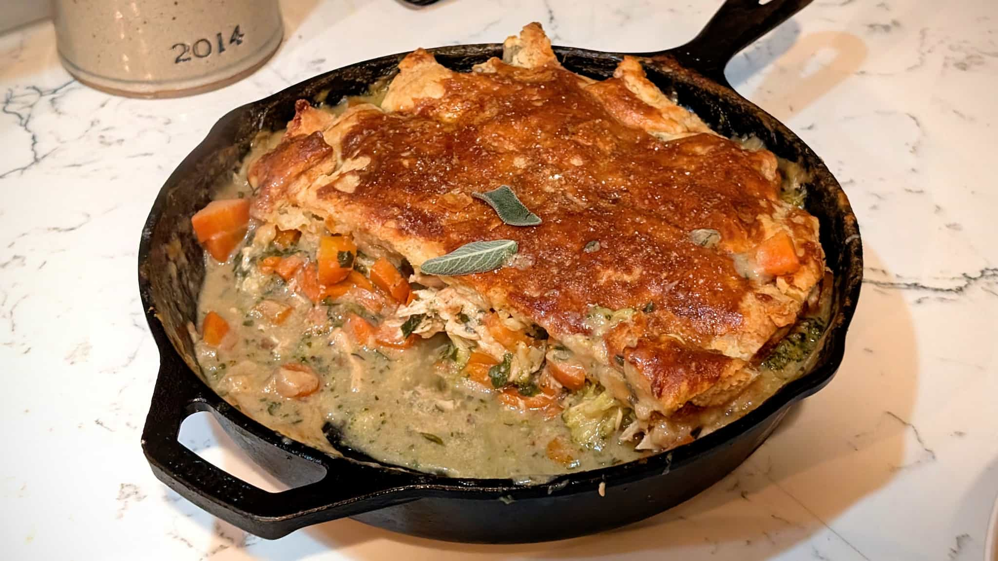 Cast iron skillet with carrots and broccoli topped with a golden pastry layer.