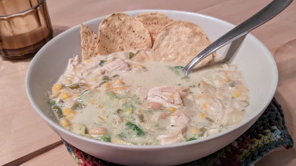 Bowl of a white soup with shredded chicken, corn, white beans, avocado, and tortilla chips.