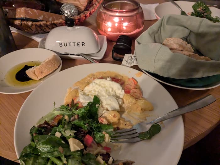 A plate with gnocchi, burrata, and salad next to candles and bread with a dipping plate.