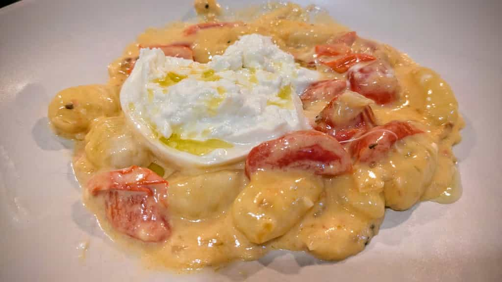 Plate of gnocchi pasta covered in a yellow sauce with cooked tomatoes.