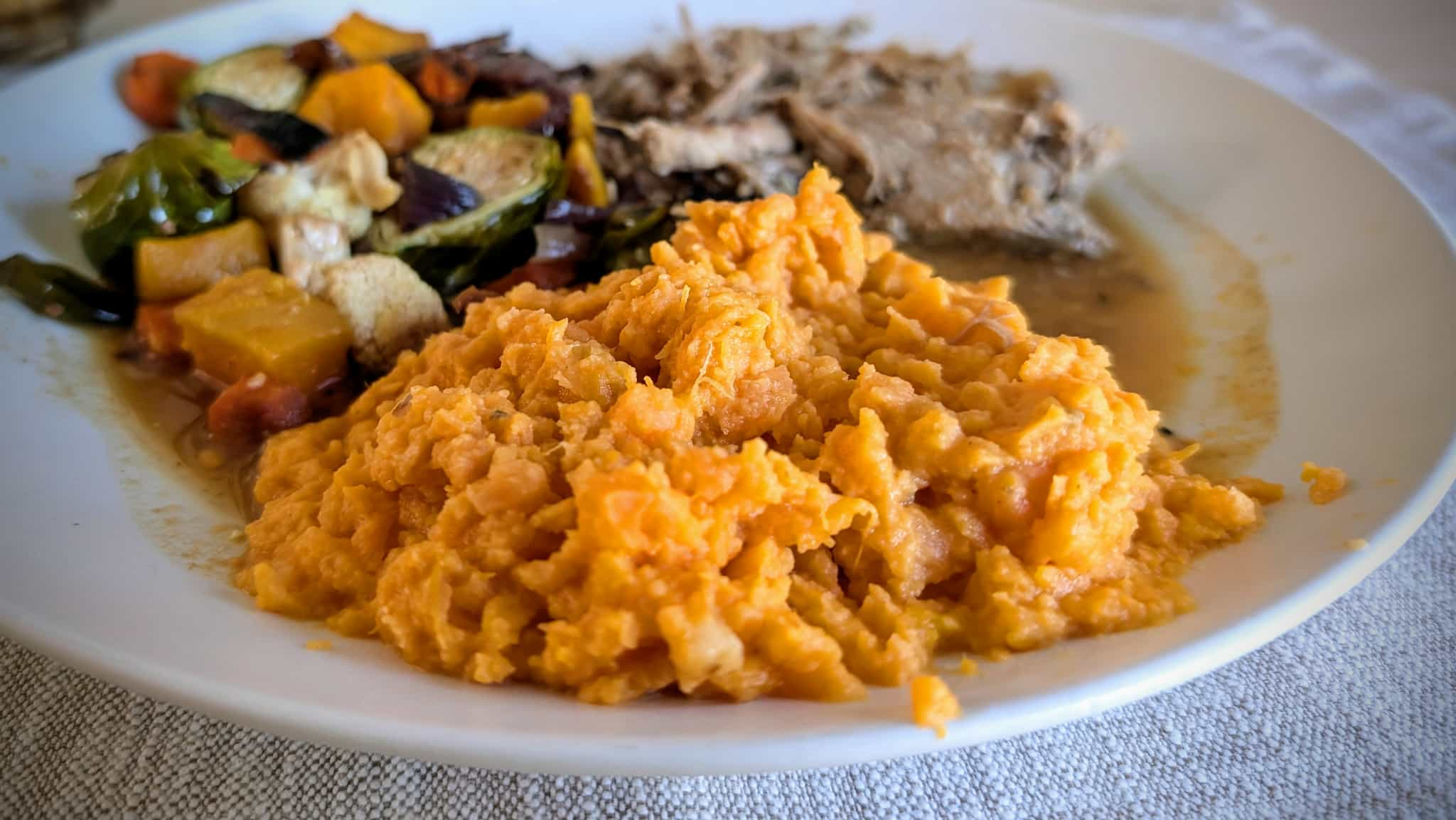 Orange mashed potatoes on a plate with pulled pork and roasted veggies.