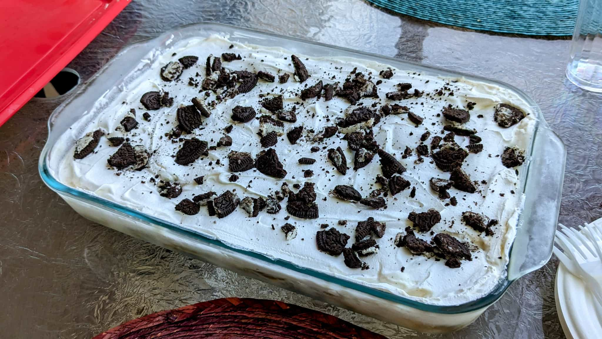 Glass pan on a picnic table filled with a white cream and topped with oreo crumbs.